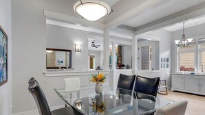 Un comedor amplio con una mesa de vidrio y sillas de cuero, una cocina moderna al fondo y un espejo grande en la pared.