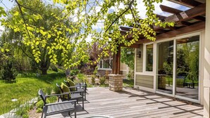 Una terraza de madera con un jacuzzi, asientos exteriores y una pérgola.