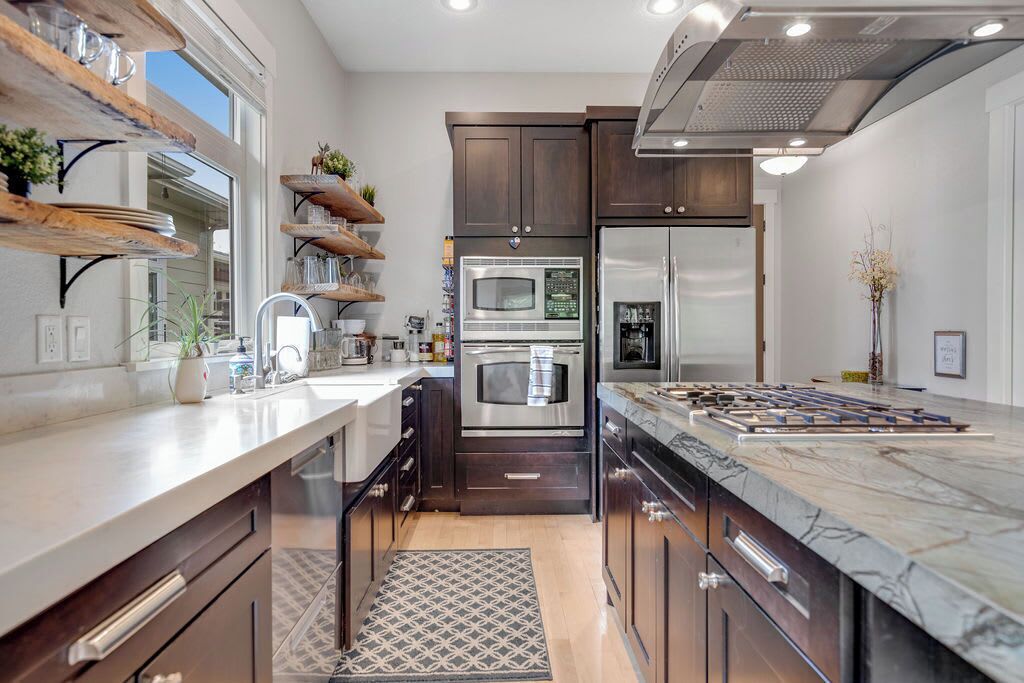 A modern kitchen with dark wood cabinets, stainless steel appliances, and a marble countertop.