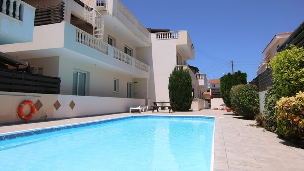 A swimming pool with a lifebuoy, a covered seating area, and a staircase leading to a balcony. - Phaedrus Living: Universal City Flat Alina (Paphos)