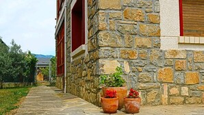Un bâtiment en pierre avec une porte rouge et une fenêtre. Devant le bâtiment, on peut voir trois plantes en pot ornées de fleurs rouges.