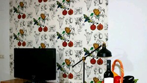 Une pièce avec un téléviseur posé sur un meuble en bois, une lampe de bureau noire, une bouteille de vin et un panier rempli de légumes.