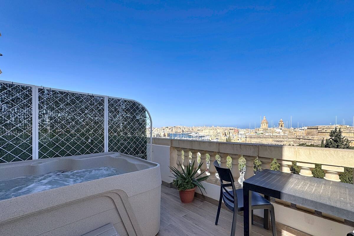Terraza en la azotea con una bañera de hidromasaje, una mesa y sillas, con vistas a un paisaje urbano con edificios históricos.