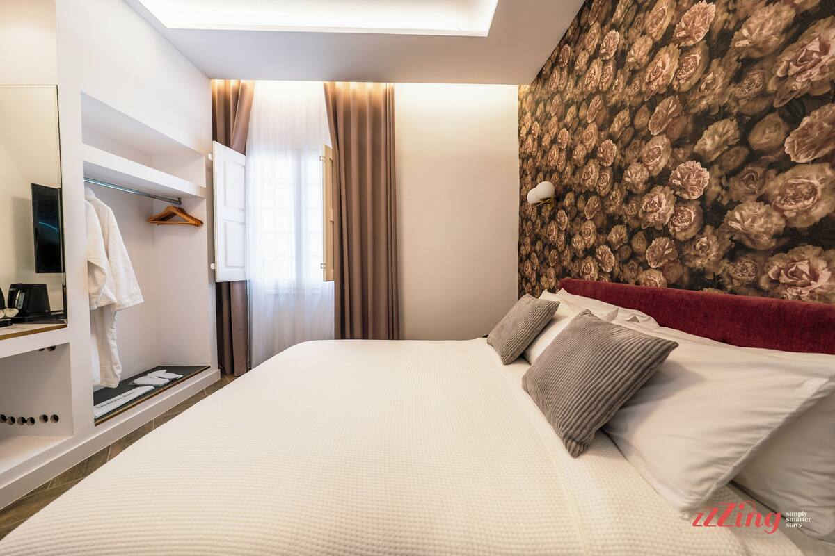 Una habitación de hotel con una cama grande, un armario con ropa colgada y un papel tapiz floral.