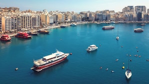 A marina with various boats, including a large cruise ship, surrounded by a cityscape with high-rise buildings. - Ta Gianni  (Sliema)