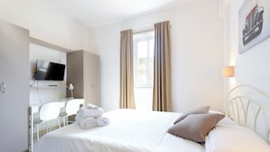 A hotel room with a bed, a desk with a TV, and a window with curtains. - Ta Gianni  (Sliema)