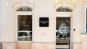 Entrada de un hotel con un letrero que dice "Stuart Rooms" y el eslogan "Duerme, relájate y repite".