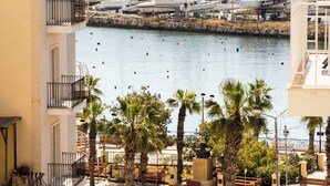 Una marina con barcos, una calle bordeada de palmeras y un edificio con balcones.