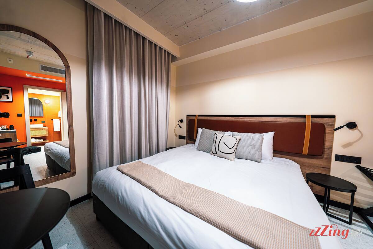 Habitación de hotel con una cama grande, un escritorio, una silla, un espejo y vistas al baño.