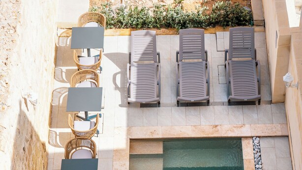 An outdoor pool area with lounge chairs and tables arranged around it. - Mosta Stays  (Mosta)
