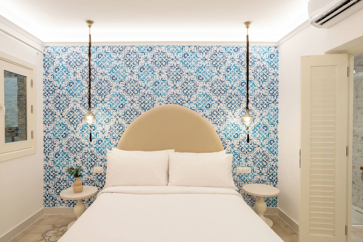 Ein Schlafzimmer mit einem großen Bett, zwei Nachttischen, einer Wand mit blauem Muster-Tapete und einer Deckenleuchte.
