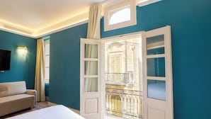 A bedroom with a bed, a sofa, a TV, and a window with a balcony view. - Mosta Stays  (Mosta)