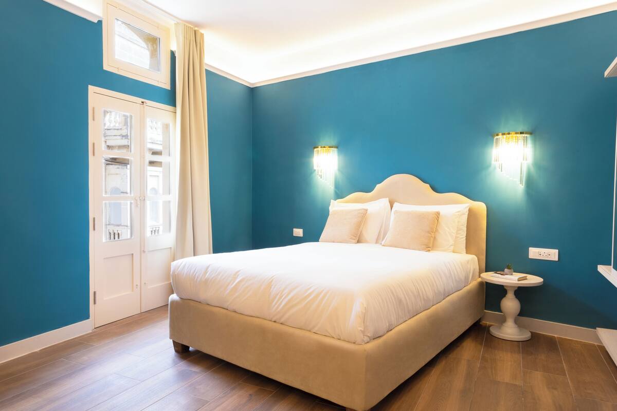 Ein Schlafzimmer mit einem großen Bett, zwei Wandleuchten, einem Nachttisch und einem Fenster mit Vorhängen.
