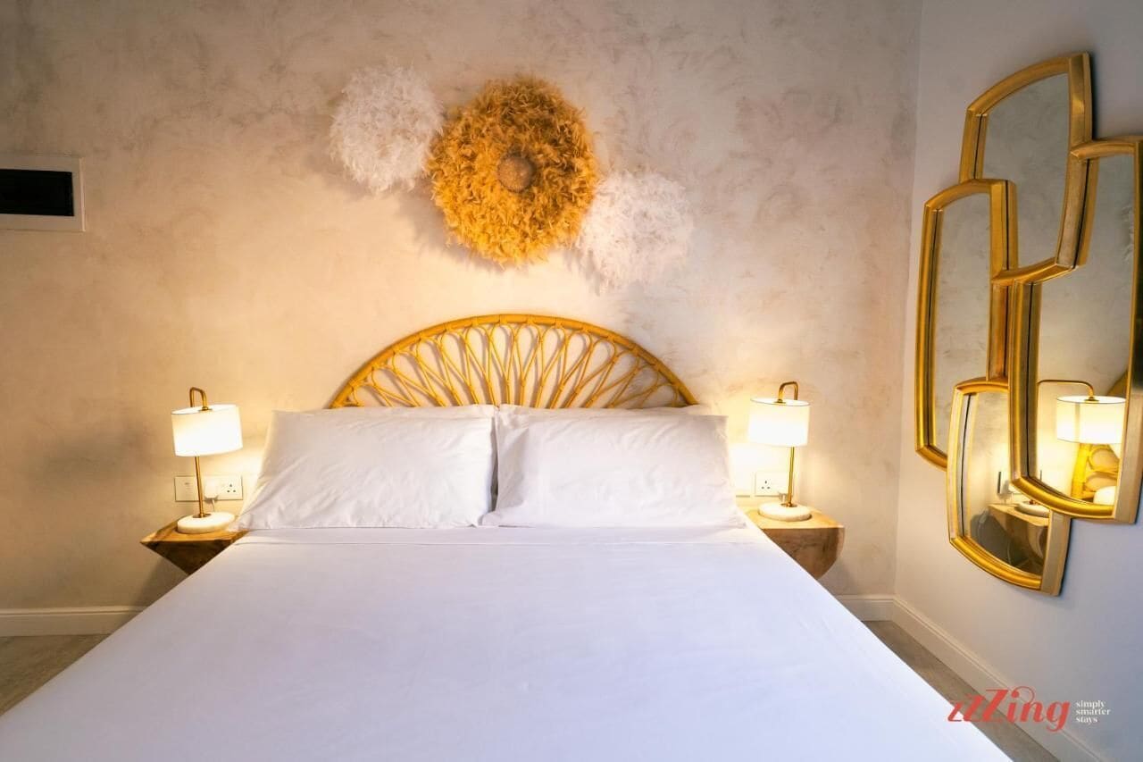 Un cuarto de hotel con una cama grande, dos lámparas de noche, un adorno en la pared y un espejo.