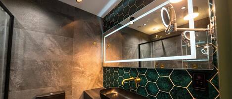 Un baño moderno con un espejo grande, un lavabo negro y un revestimiento de azulejos hexagonales.