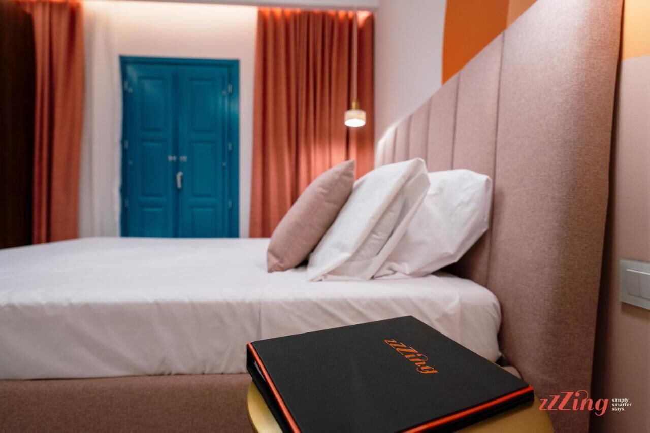 Un letto rifatto con cuscini, un libro nero su un comodino e una porta blu sullo sfondo.