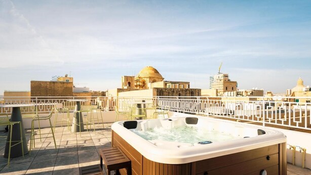 A rooftop terrace with a hot tub, outdoor seating, and a view of historic buildings.