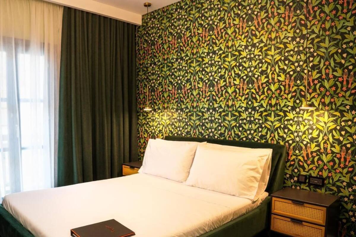 A hotel room with a bed, a nightstand, a lamp, and a window with curtains.