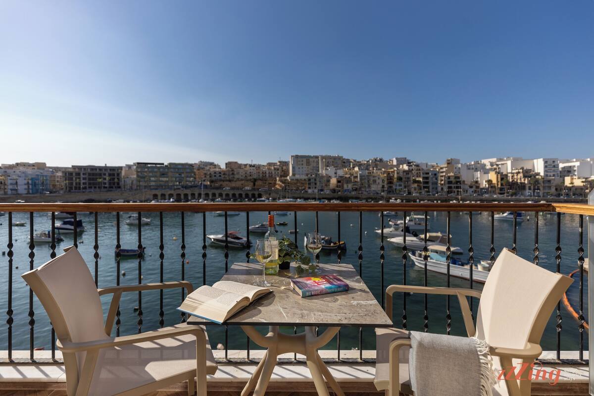 Un balcone con un tavolo, due sedie e vista su una marina con barche ed edifici.