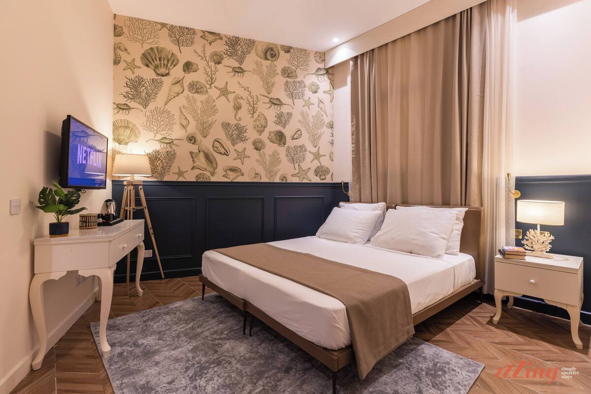 Camera d'albergo con un letto, una scrivania, una TV e una parete decorata con un motivo a foglia.