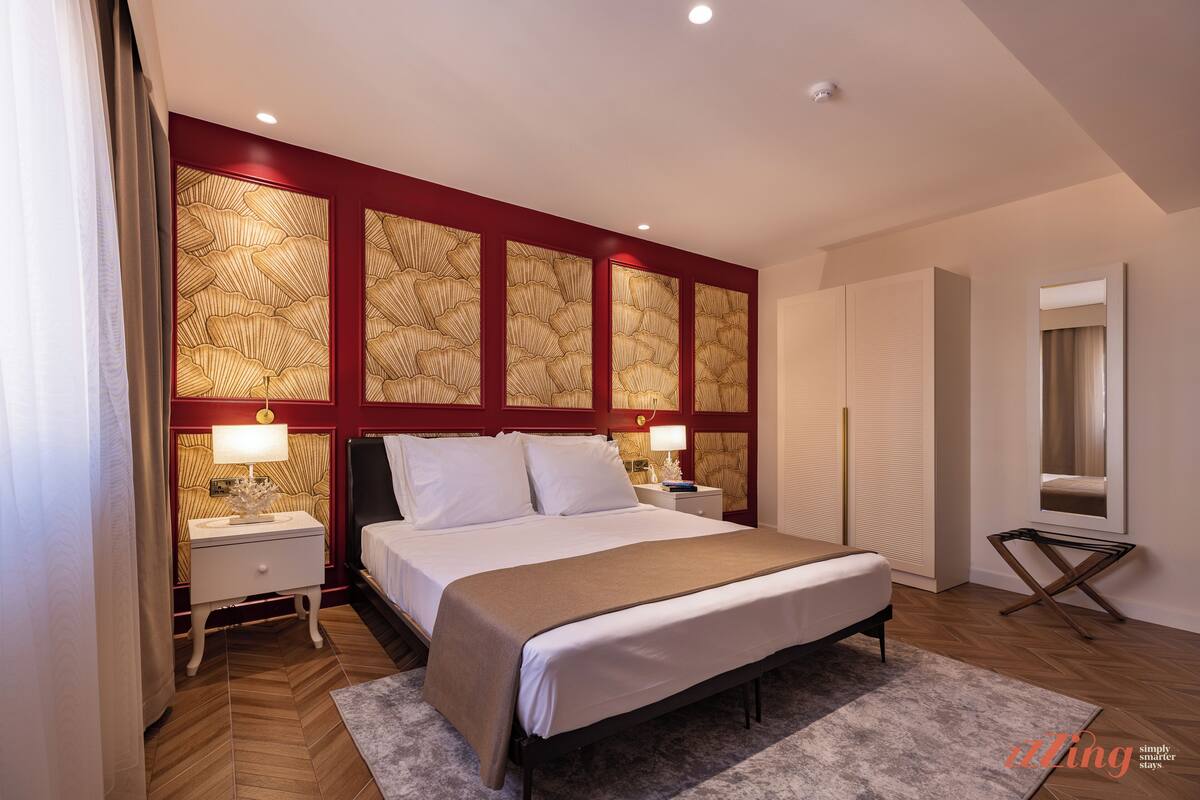 Una camera da letto moderna con un letto grande, due comodini con lampade, una testiera decorativa e un piccolo tavolino.