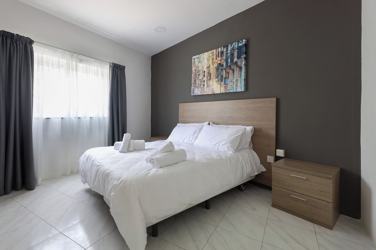 Ein modernes Hotelzimmer mit einem großen Bett, einem hölzernen Kopfteil, einem Nachttisch mit Schubladen und einem Gemälde an der Wand.