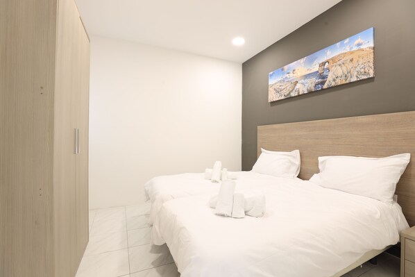 Une chambre d’hôtel avec deux lits, une armoire en bois, un tableau au mur et un sol carrelé.