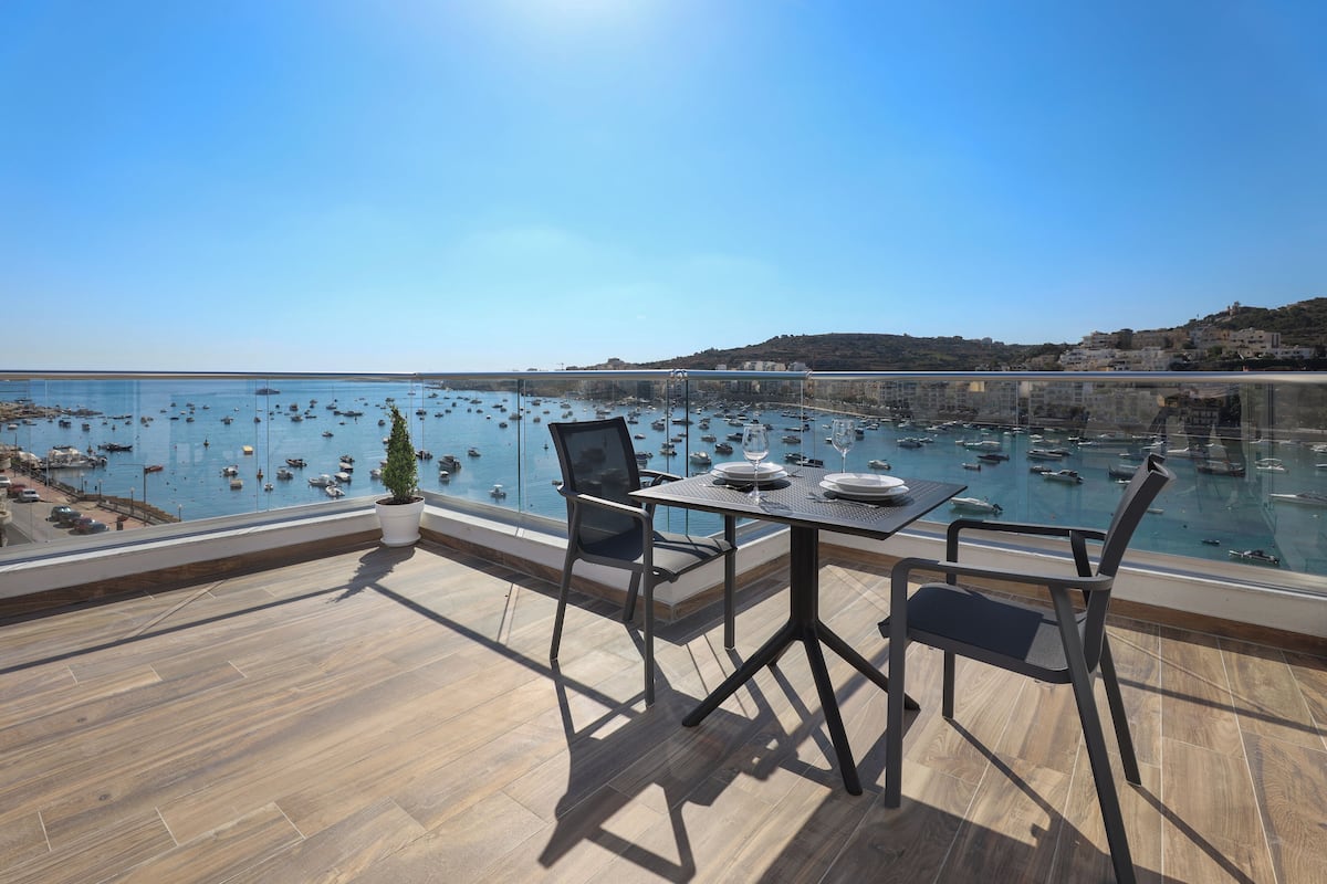 Eine Terrasse mit Tisch und Stühlen mit Blick auf eine Marina und Boote.