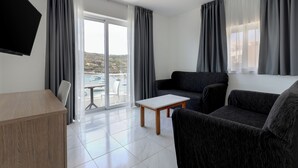 Una sala moderna con un sofá, una mesa de centro y un televisor. Hay una puerta corrediza de vidrio que da a un balcón con vistas a la ciudad.