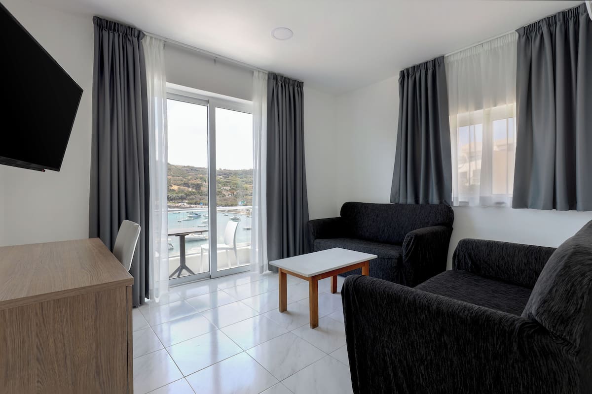 Ein modernes Wohnzimmer mit einer Couch, einem Couchtisch und einem Fernseher. Eine Glastür öffnet sich zu einem Balkon mit Blick auf die Stadt.