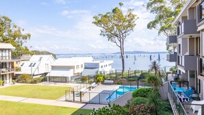 Ett bostadsområde med en swimmingpool, utsikt över havet med segelbåtar och moderna byggnader.
