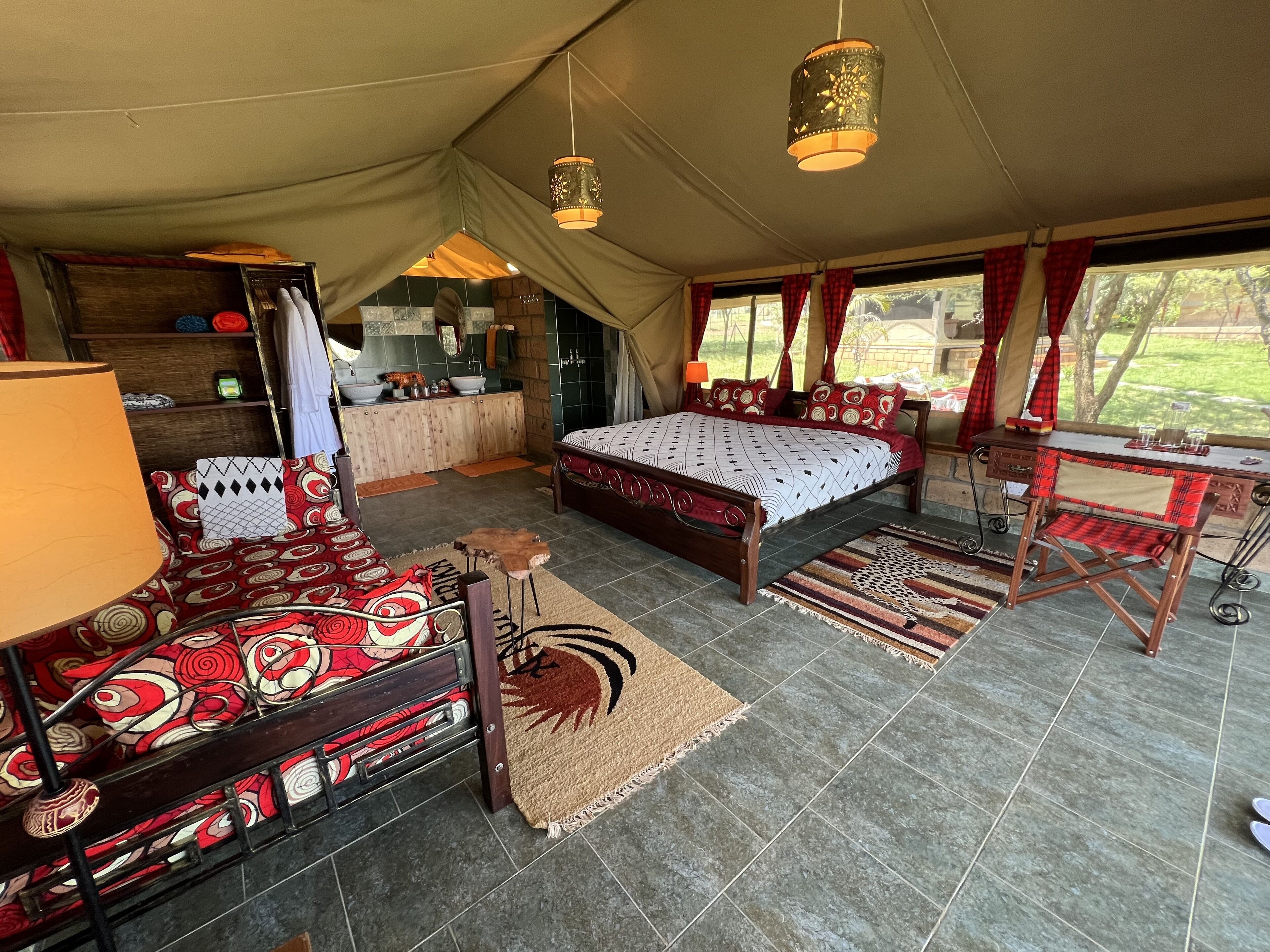 A tented accommodation with a bed, a desk, a lamp, and a bathroom area.