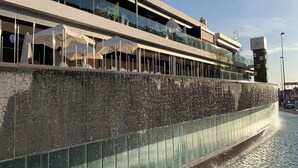 Ein Gebäude am Wasser mit einem Restaurant namens "Gastro Gallery" und einer Terrasse mit Sonnenschirmen.