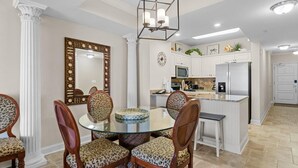 Zona pranzo con tavolo in vetro circondato da quattro sedie con cuscini a leopardati, uno specchio decorativo e una lampada a sospensione moderna.