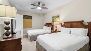 Une chambre d’hôtel avec deux lits simples, un ventilateur de plafond, un bureau avec une lampe et un téléviseur.
