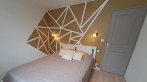 A bedroom with a bed, a geometric wall design, and a door. - Gite des Falaises de Longues 6 p (Longues-sur-Mer)