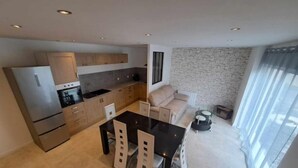A modern kitchen with a dining area, a stone wall, and a large window. - Gite des Falaises de Longues 6 p (Longues-sur-Mer)