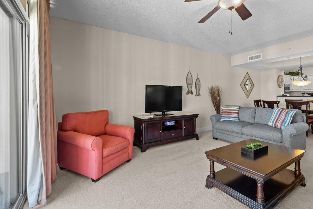 Un salon avec un canapé rouge, un canapé gris, un téléviseur posé sur un meuble en bois et un ventilateur de plafond.