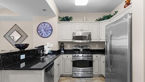 Una cocina moderna con armarios blancos, un refrigerador de acero inoxidable, un microondas, una estufa y un reloj en la pared.