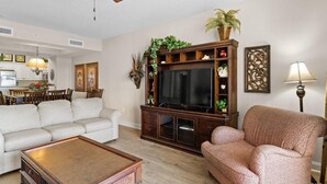 Una sala de estar con sofá, sillón, mesa de centro, mueble para televisor con adornos y una lámpara.
