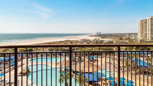 Un hotel con varias piscinas, vista a la playa y un rascacielos al fondo.
