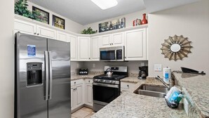 Una cocina moderna con armarios blancos, electrodomésticos de acero inoxidable, encimeras de granito y un espejo decorativo.