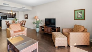 A living room with a flat-screen TV, two patterned armchairs, a coffee table, and a potted plant. - Sunset Symphony Luxurious 2BR/2BA Oceanfront Condo (North Myrtle Beach)