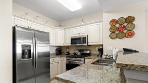 A modern kitchen with stainless steel appliances, white cabinetry, granite countertops, and a decorative wall art piece.