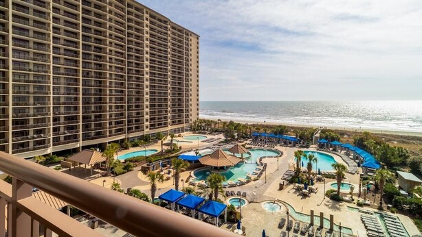 A hotel with a large building and a pool area with multiple pools and lounge chairs. - Wave Watcher's Paradise Cove: 2BR Condo (North Myrtle Beach)