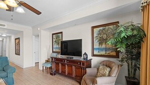 Un salon avec un téléviseur, un canapé, un fauteuil et une grande plante en pot.