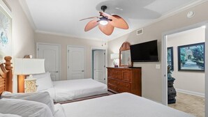 Une chambre avec deux lits, un ventilateur de plafond, une télévision et une commode.