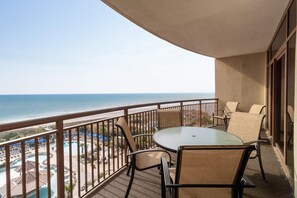 Un balcon avec une table et des chaises, donnant sur une piscine et une plage.
