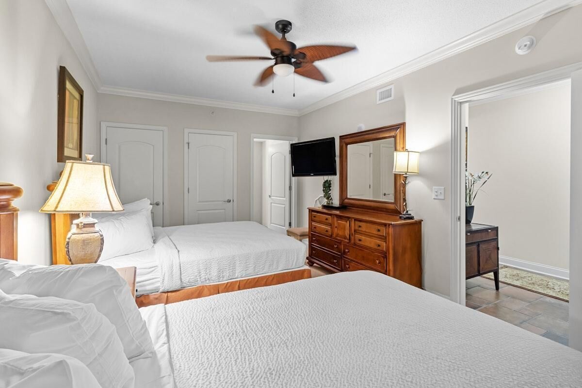 Une chambre d’hôtel avec deux lits, un ventilateur de plafond, une télévision, une commode et un miroir.
