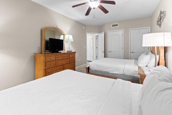 A bedroom with two beds, a wooden dresser, a ceiling fan, and a mirror.